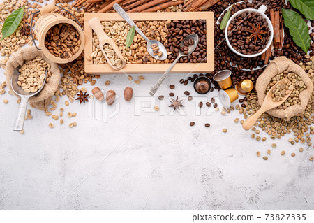 Green and brown decaf unroasted and dark roasted coffee beans in wooden box with scoops setup on white concrete background. Green and brown decaf unroasted and dark roasted coffee beans in wooden box with scoops setup on white concrete background. 73827335