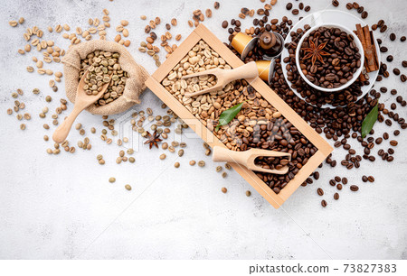 Green and brown decaf unroasted and dark roasted coffee beans in wooden box with scoops setup on white concrete background. Green and brown decaf unroasted and dark roasted coffee beans in wooden box with scoops setup on white concrete background. 73827383