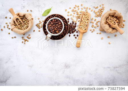 Green and brown decaf unroasted and dark roasted coffee beans in hemp sack bags with scoops setup on white concrete background. Green and brown decaf unroasted and dark roasted coffee beans in hemp sack bags with scoops setup on white concrete background. 73827394