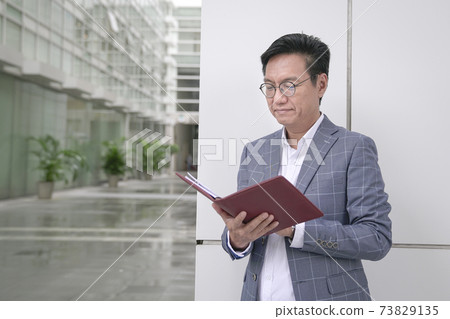 Businessman standing and looking at his appointment book. 73829135