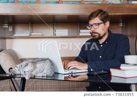 Working at home with pet laying on lap. Man works from home typing on laptop. 73831955
