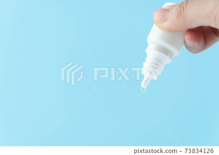 Female hand holding eye drop or ear drop bottle with droplet on blue background. Pharmaceutical product. Copy space. Female hand holding eye drop or ear drop bottle with droplet on blue background. Pharmaceutical product. Copy space. 73834126