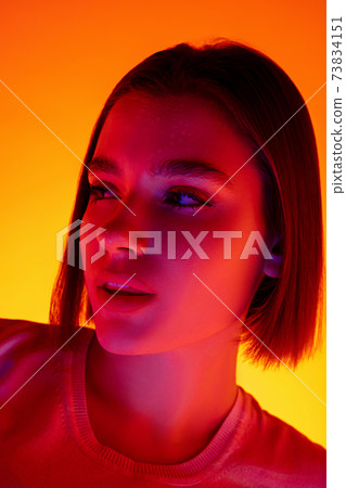 Caucasian woman's portrait isolated on orange studio background in multicolored neon light 73834151