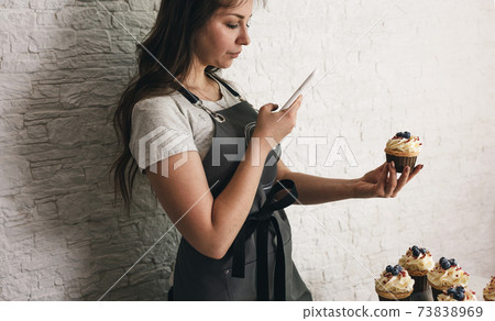 A girl blogger takes photos on her phone of delicious cakes and cupcakes for her subscribers. 73838969