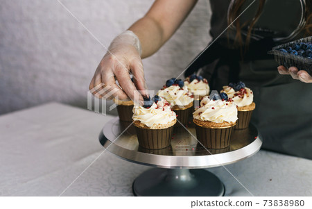 the chef girl decorates fresh cupcakes covered with vanilla cream with berries.Sweet homemade cupcakes with cream on a tray. Food for breakfast. Freshly baked cupcakes for dessert. the chef girl decorates fresh cupcakes covered with vanilla cream with berries.Sweet homemade cupcakes with cream on a tray. Food for breakfast. Freshly baked cupcakes for dessert. 73838980