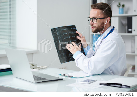 Confident doctor pointing at x-ray image of patient during online consultation Confident doctor pointing at x-ray image of patient during online consultation 73839491