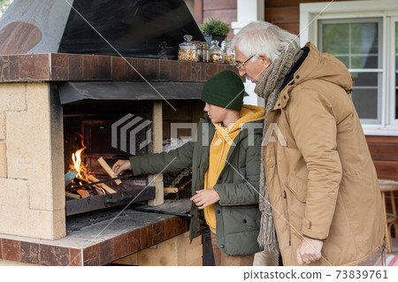 Cute youngster or teenager in warm jacket and beanie standing by fireplace Cute youngster or teenager in warm jacket and beanie standing by fireplace 73839761