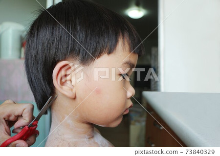 Little Asian boy cut hair in a room by his mother at the time of the coronavirus outbreak. 73840329
