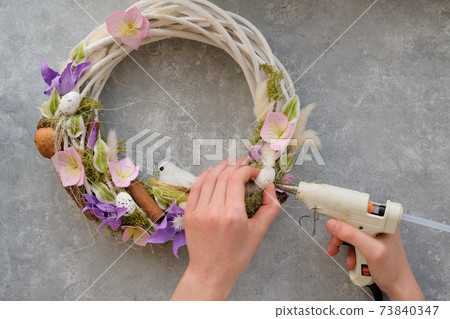 A faceless woman creates an Easter wreath, glues with a glue gun. The A faceless woman creates an Easter wreath, glues with a glue gun. The 73840347