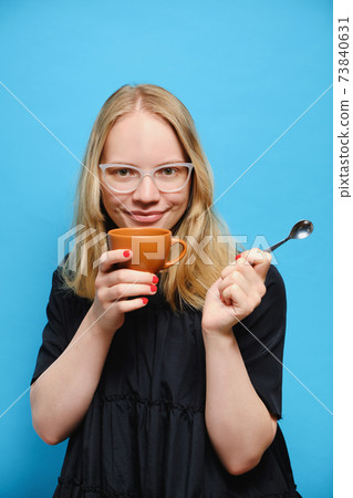 Young cheerful Caucasian girl holding a cup and spoon in her hands and Young cheerful Caucasian girl holding a cup and spoon in her hands and 73840631