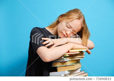 Tired Caucasian girl student laid her head and sleeps on a stack of Tired Caucasian girl student laid her head and sleeps on a stack of 73840633