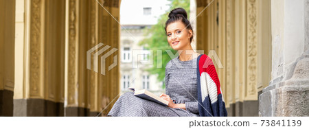 Student with book sitting on stairs Student with book sitting on stairs 73841139