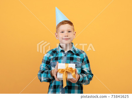 Smiling birthday boy holding present, yellow background 73841625