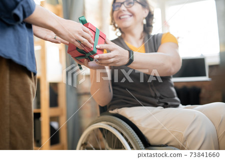 Young cheerful disable businesswoman passing giftbox with present to colleague 73841660