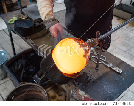 Man Hands Shaping hot glass art piece with wooden tool 73844698