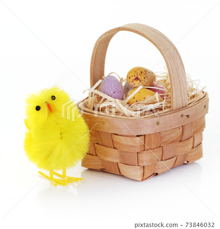 Easter chick and candy eggs in a basket with straw on white 73846032