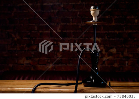 Classic black hookah stands alone on a wooden table with a brick wall in the background  73846033