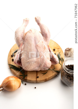 Fresh whole chicken on a cutting board with pepper, parsley, onion and garlic. Fresh whole chicken on a cutting board with pepper, parsley, onion and garlic. 73847962