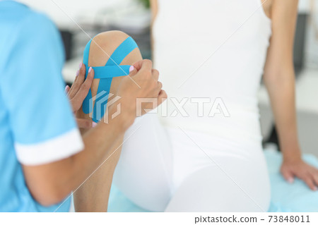 Doctor fixes kinesio tape on patient's leg Doctor fixes kinesio tape on patient's leg 73848011