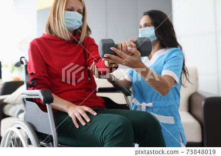 Doctor helps woman in wheelchair to do exercises with dumbbells Doctor helps woman in wheelchair to do exercises with dumbbells 73848019