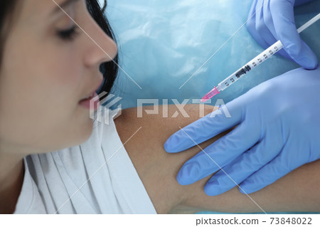 Doctor gives woman an injection in shoulder 73848022
