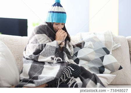 Frozen woman in hat and blanket sits on couch Frozen woman in hat and blanket sits on couch 73848027
