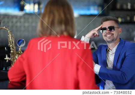Smiling confident man in sunglasses meets woman near bar counter 73848032