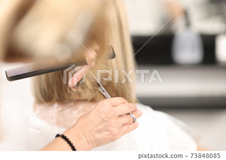 Hairdresser holds comb and scissors in his hands and cuts client's hair Hairdresser holds comb and scissors in his hands and cuts client's hair 73848085