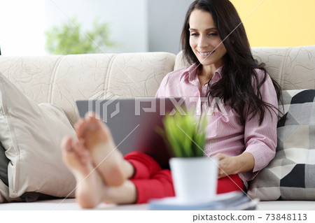Woman is sitting on couch and working on laptop 73848113