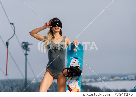 Attractive woman dressed in swimsuit with snowboard on the slope 73848270