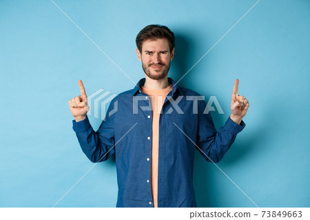 Skeptical young man frowning and squinting, cringe from something disgusting, standing on blue background 73849663