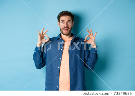 Impressed man praising something awesome, showing okay signs and looking amazed, complimenting good thing, standing on blue background 73849686