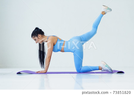 Warming up before training. Beautiful young woman in sportswear doing stretching at white interior fitness club. 73851820