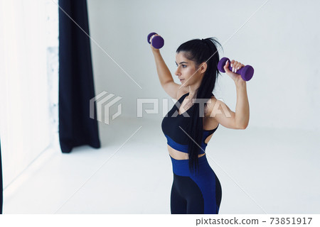 Young beautiful woman doing exercises with dumbbells in fitness studio. Athletic girl enjoying her training process. 73851917