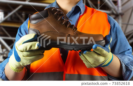 Worker in orange jacket outfit holding boot. 73852618