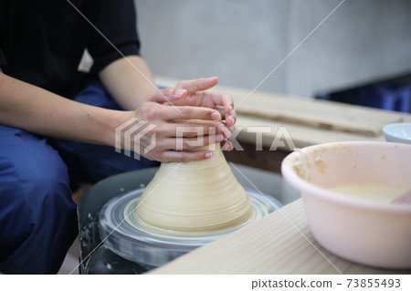 A man's hand beyond the elbow that turns the potter's wheel 73855493
