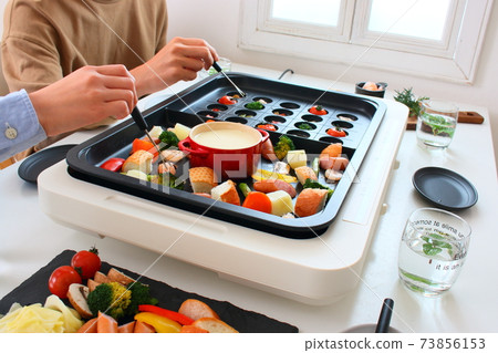 Family dining table with ajillo and cheese fondue on a hot plate 73856153