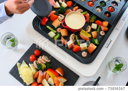 Family dining table with ajillo and cheese fondue on a hot plate 73856167
