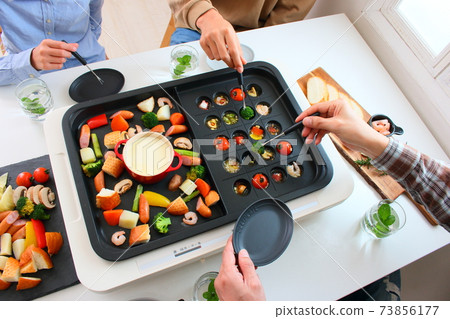 Family dining table with ajillo and cheese fondue on a hot plate 73856177
