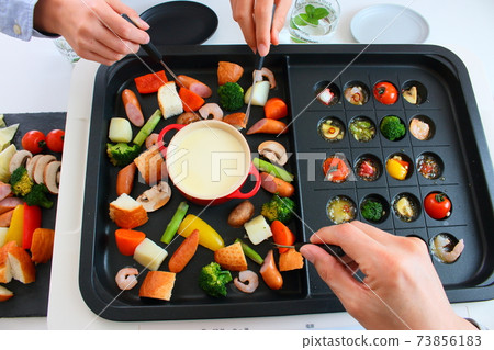 Family dining table with ajillo and cheese fondue on a hot plate 73856183