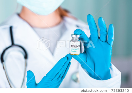 Woman doctor or nurse in uniform and gloves wearing face mask protective in lab holding medicine vial vaccine bottle with COVID-19 Coronovirus vaccine label Woman doctor or nurse in uniform and gloves wearing face mask protective in lab holding medicine vial vaccine bottle with COVID-19 Coronovirus vaccine label 73863240