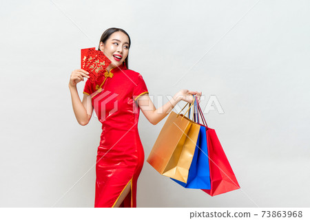 Asian woman in traditional dress holding bags and red envelopes 73863968
