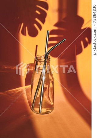Reusable Metal Straws in glass bottle with water on yellow background with plant shadow - Stainless Steel, Eco-Friendly Drinking Straw Set. Zero waste. Plastic free. 73864830