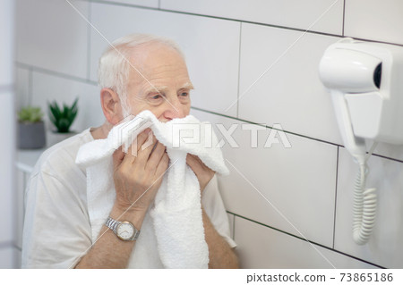 Gray-haired man in white tshirt wiping his face with the towel 73865186
