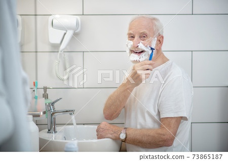 Gray-haired man in white tshirt shaving in the bathroom 73865187