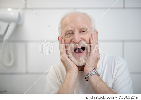 Gray-haired man in white tshirt touching his face Gray-haired man in white tshirt touching his face 73865279