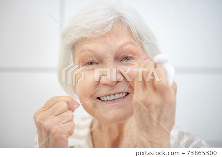 Gray-haired woman cleaning her teeth and using floss Gray-haired woman cleaning her teeth and using floss 73865300