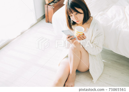 一個女人在房間裡喝咖啡時看著她的智能手機 一個女人在房間裡喝咖啡時看著她的智能手機 73865561