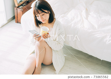 一個女人在房間裡喝咖啡時看著她的智能手機 一個女人在房間裡喝咖啡時看著她的智能手機 73865562