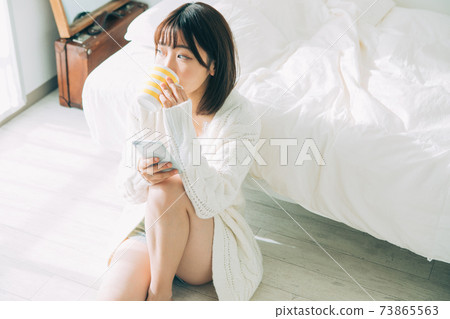 A woman looking at her smartphone while drinking coffee in the room 73865563